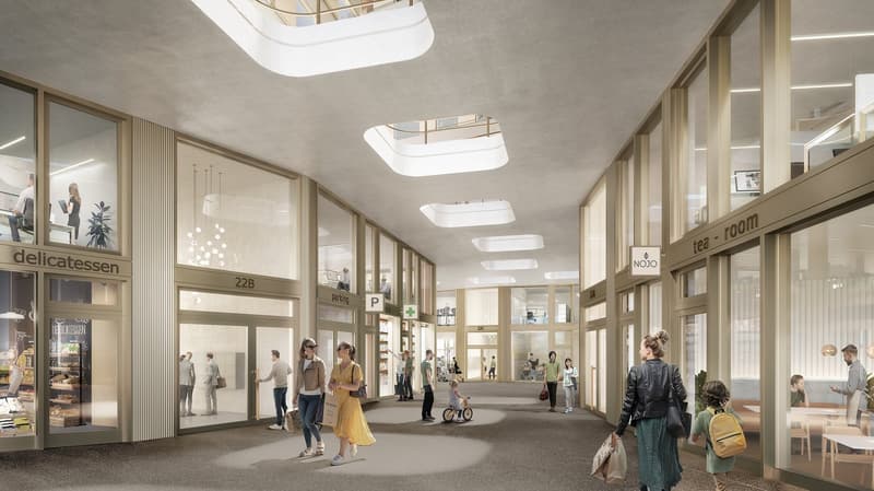 Indoor shopping area with a delicatessen, tea room, and various other shops. The space has high ceilings with skylights, glass walls, and people walking around the area.