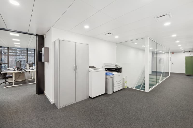 minimalistic office room, grey carpeting, white walls, desk with monitor, office chair, glass partition, stairs