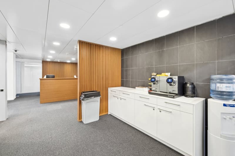 Modern office with reception desk, trash bin, white cabinets, and a water dispenser.