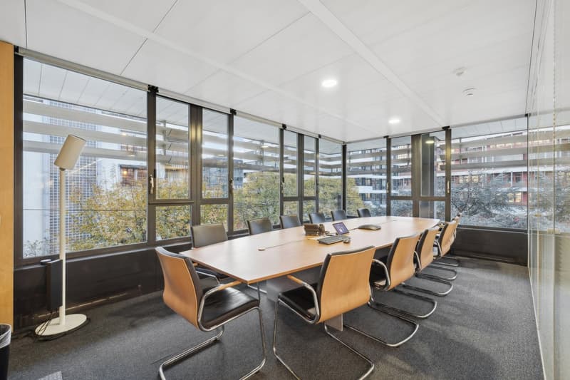 modern office room, large windows, conference table with chairs, equipment, trash can, view of city outside
