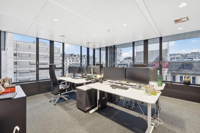 an empty office space with desks, chairs, monitors, bottles, and a view of a city outside
