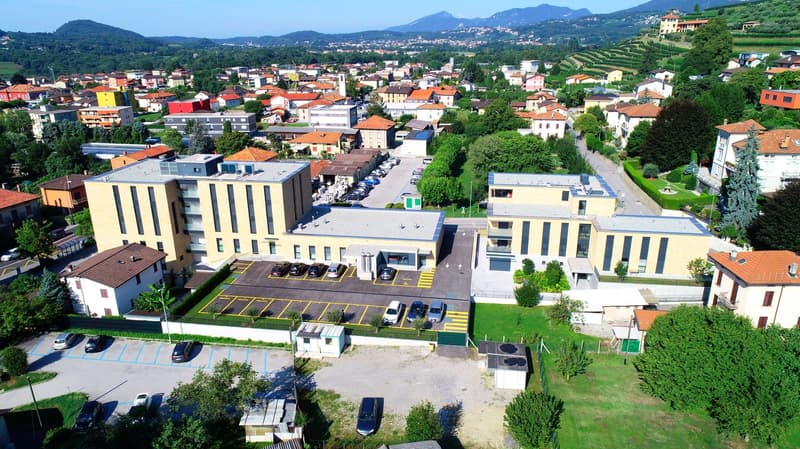Large building with multiple car parks in front and to the sides, surrounded by trees and hills