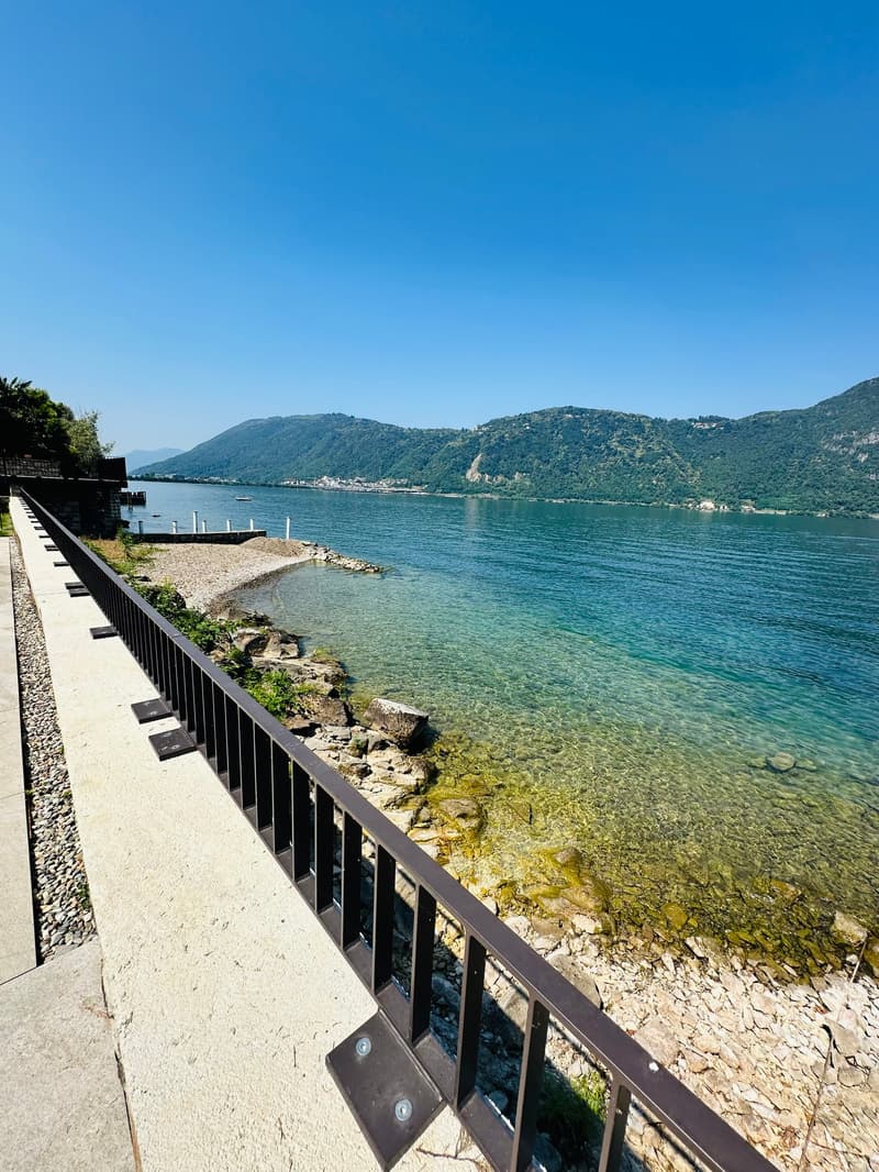 Pathway with railings, rocky shore, clear water, mountains in the distance