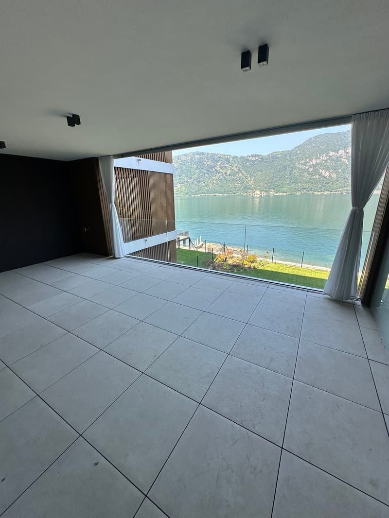 large balcony with glass railing, tiled floor, white curtains, view of lake and mountains