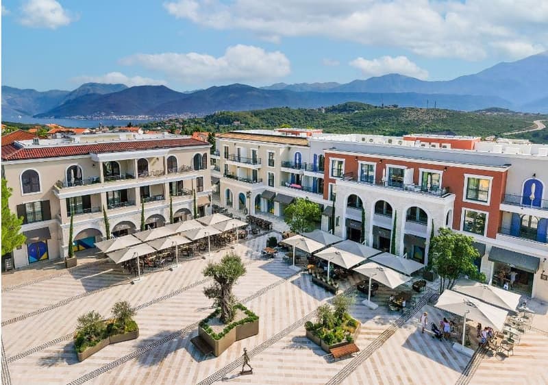 aerial view of a shopping plaza with various buildings, mountains in the distance