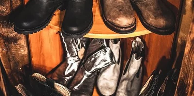 The image shows a mudroom or entryway with various pairs of boots and shoes stored on shelves. The boots appear to be work or outdoor boots, suggesting this is a space for storing and organizing footwear, likely in a garage or similar utilitarian area.