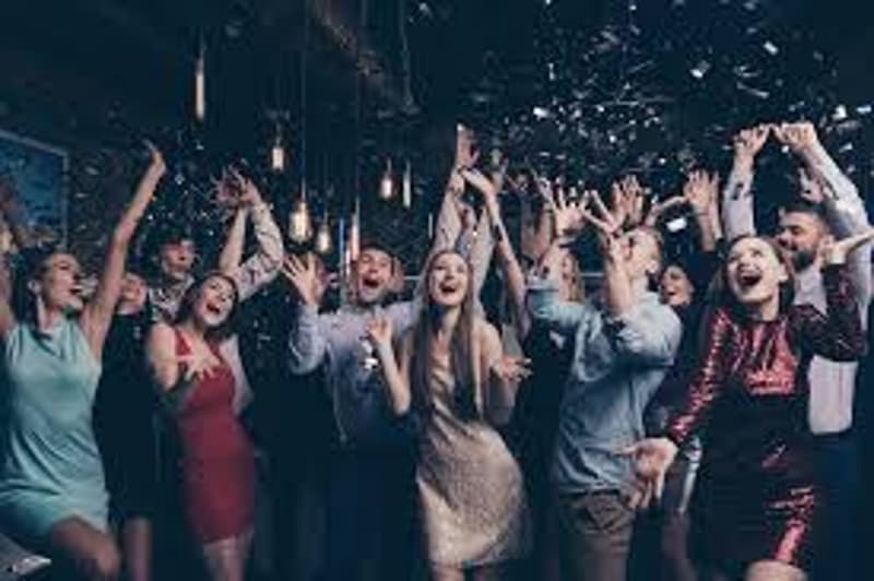 A group of people celebrating at a party, with confetti in the air and their arms raised in excitement.