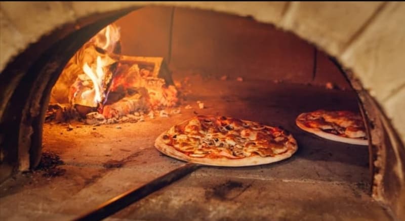 A traditional brick pizza oven with a fire burning inside, and two freshly baked pizzas on the oven floor