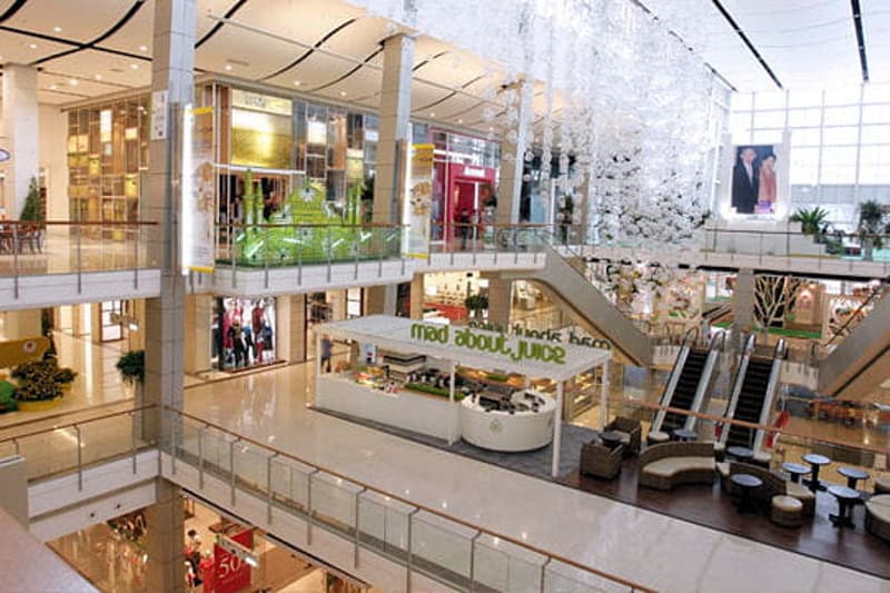 Large indoor shopping mall with multiple levels, glass walls, and various retail stores and shops visible.