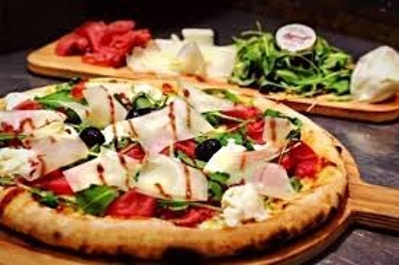 Pizza with cheese, tomatoes, olives, and greens on a wooden board