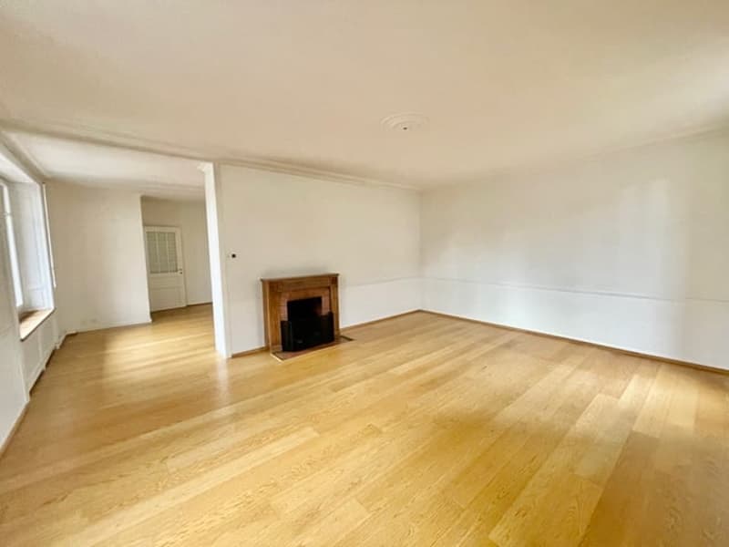 Spacious living room with hardwood floors, white walls, and a fireplace