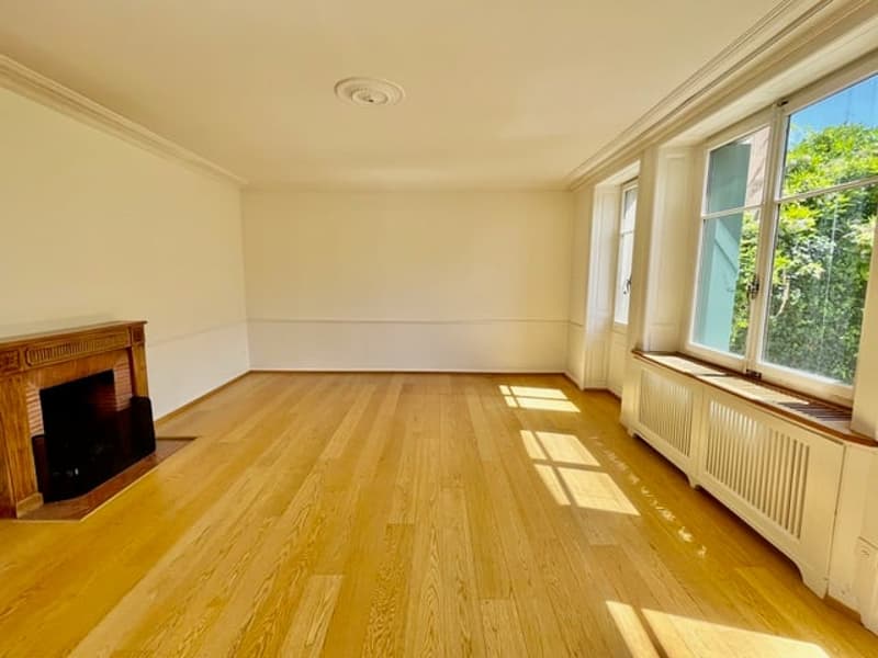 Spacious living room with hardwood floors, large windows, and a fireplace
