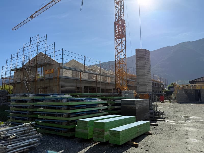 Building under construction with scaffolding and a crane, surrounded by building materials