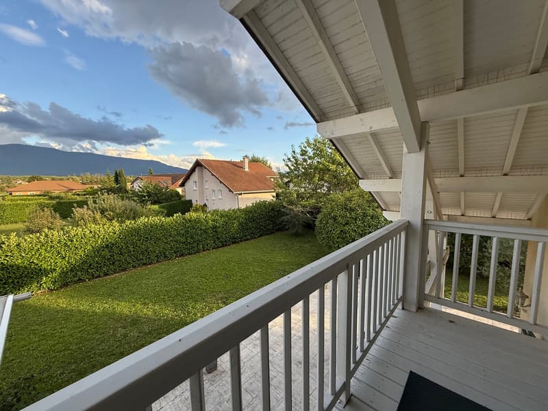 wooden floor, white railings, large glass windows, rug, grassy landscape, trees, houses, mountains