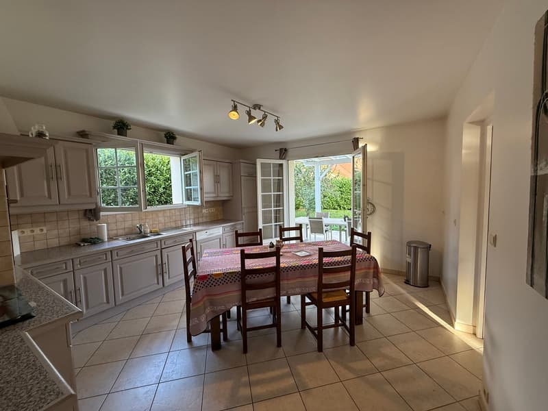 Table with chairs, wooden dining table, white walls, tiled floor, kitchen, open balcony with tables and chairs, plants on cabinet