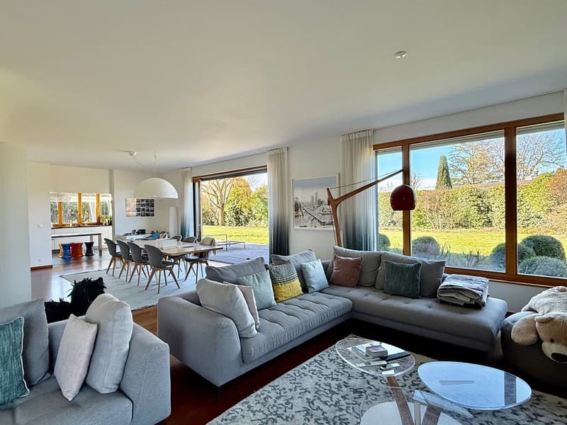 large L-shaped sofa, glass tables, carpet, large windows, glass sliding door, garden view