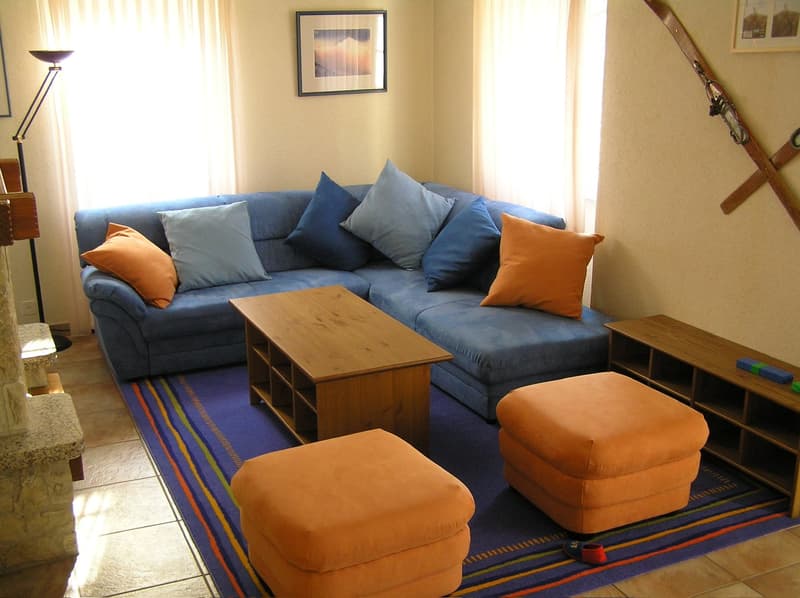 living room, blue sofa, wooden coffee table, blue rug, two orange footstools, two large cushions, fireplace