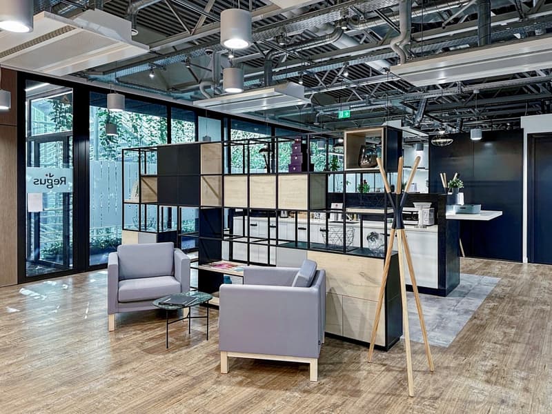 Open concept office space with large windows, exposed ceiling, modular furniture, and storage units. The space has a modern and industrial design aesthetic.