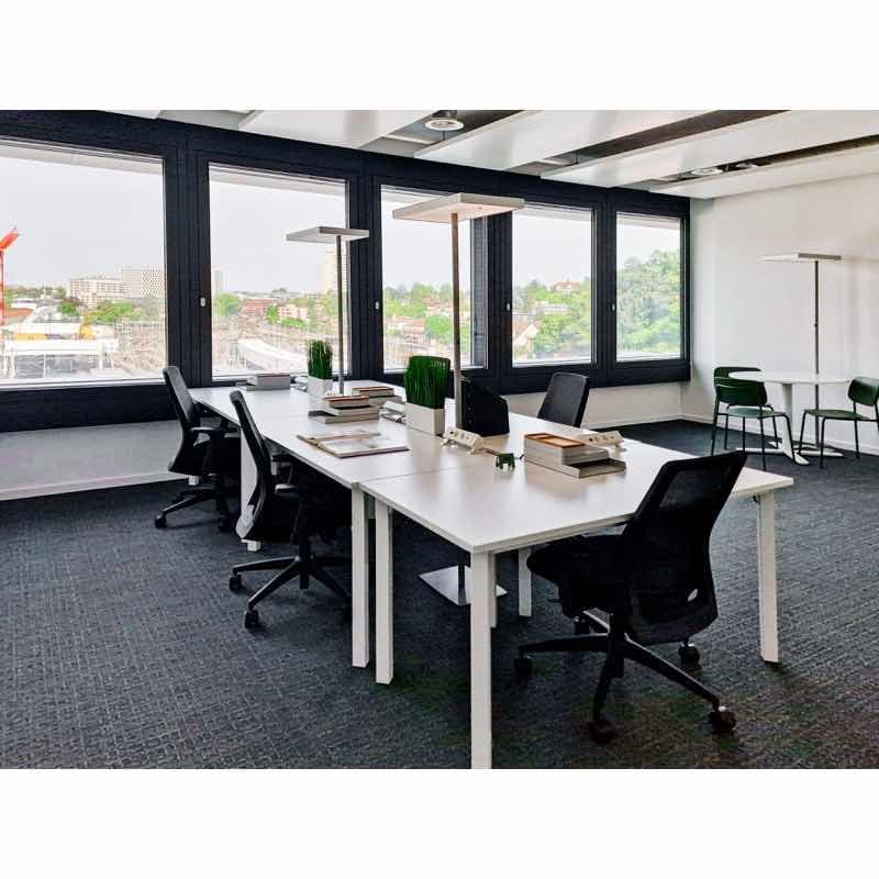modern office room, large windows, carpeted floor, white desks, black swivel chairs, bookshelves, white table, green chairs