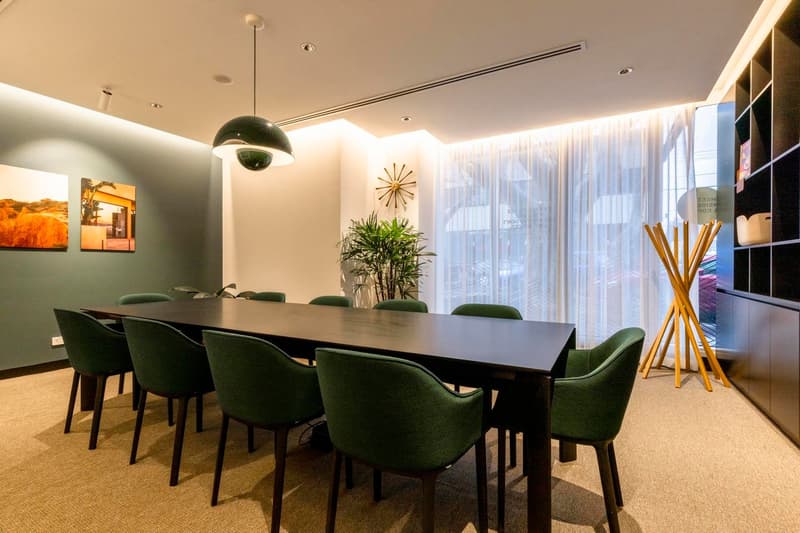 Large dining table with green upholstered chairs, pendant light fixture, artwork on the walls, potted plant, and a fireplace visible in the room.