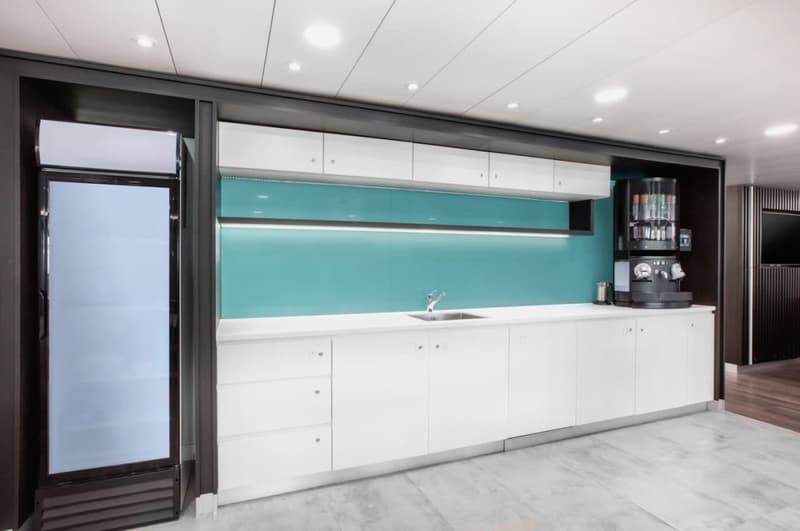 Modern, open-concept kitchen with white cabinets, teal backsplash, stainless steel appliances including a dishwasher, and large windows providing natural light.