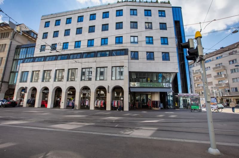 white and blue facade building, many windows, arched entrance, retail stores on the ground floor
