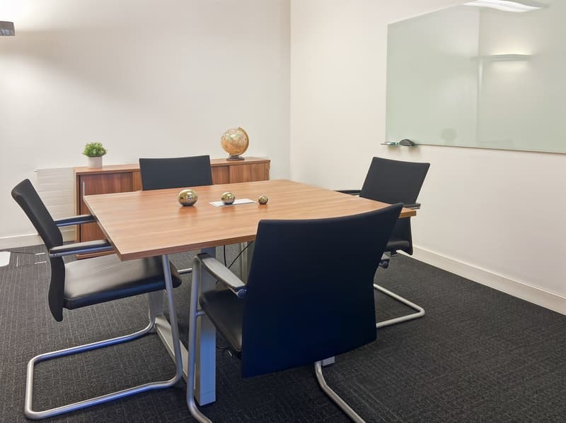 The image shows a modern office space with a wooden conference table, black leather chairs, a sideboard with decor items, and a large mirror on the wall. The room has a minimalist and professional design with neutral colors and clean lines.