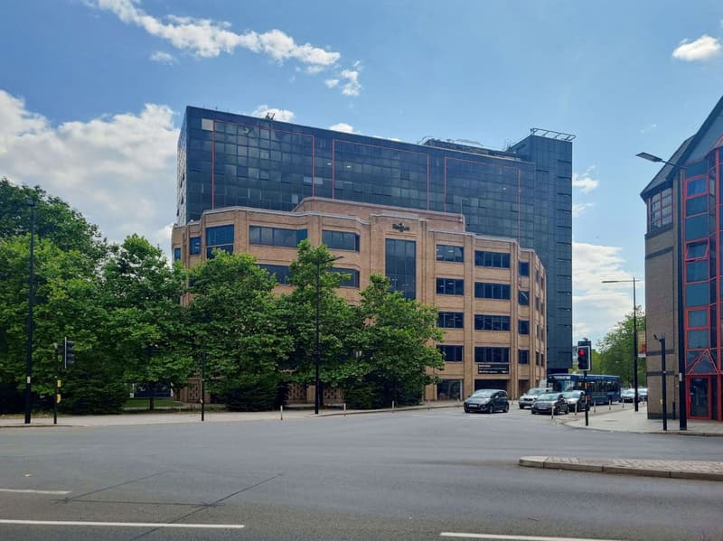 High-rise building with brick base and glass walls, several parked cars, streetlights, and trees