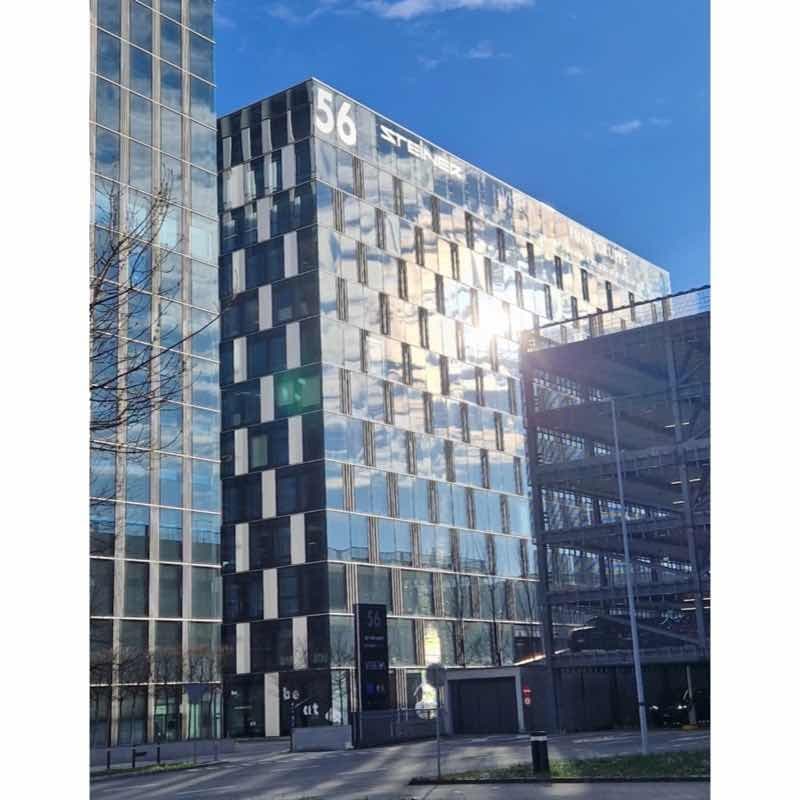 Modern office building with reflective glass facade, multi-level parking, situated on a busy road.