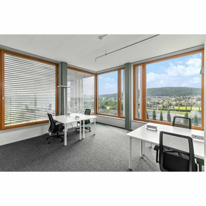 Office room with large windows, white desks, black chairs, gray carpet, large view of the outside landscape.