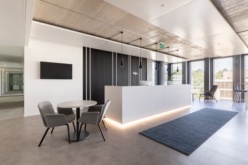 modern open space with glass walls, white furniture, tiled floor, round table, chairs, and a blue rug