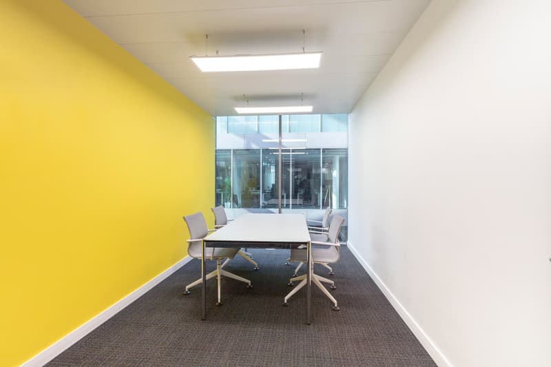 empty meeting room, yellow wall, white wall, long table, 6 chairs, carpeted floor, fluorescent ceiling lights