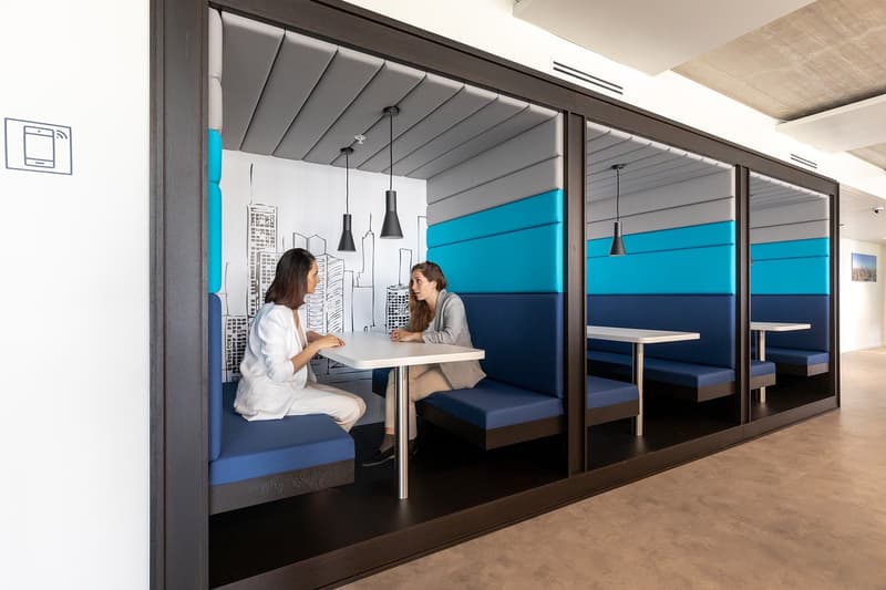 enclosed seating area with bench seating, round tables, white walls, grey and blue accent colors, hanging lamps