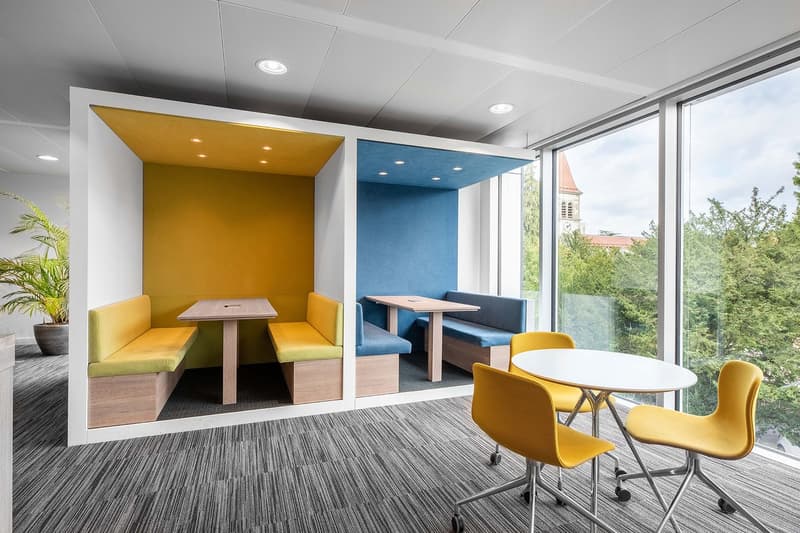 modern office room with yellow and blue booths, tables, chairs, carpet, and large windows