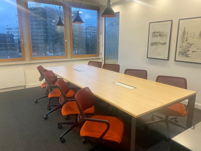long wooden table, red chairs, large windows, two framed pictures on the wall, radiator