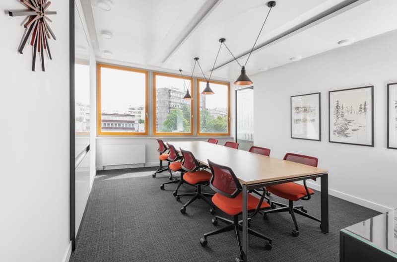 empty meeting room with long table, red chairs, white walls, large windows, ceiling lamps, clock, framed pictures