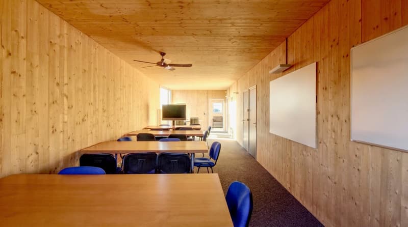 Wooden walls, wooden ceiling, wooden tables, blue chairs, whiteboards, ceiling fan, television
