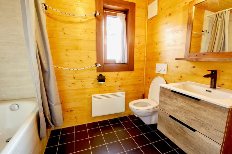 Bathroom with wooden walls, bathtub, toilet, sink, mirror, and window.