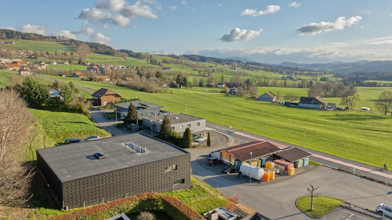 Aerial view of a rural area with several houses, a road, and a parking lot with cars parked.