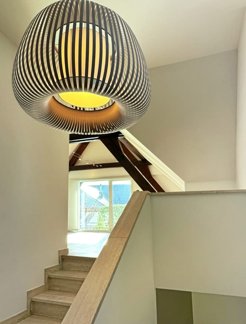 Modern staircase, wooden handrail, central spiral light fixture, window with exterior view