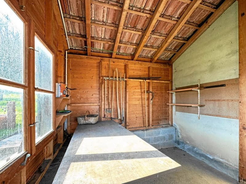 Wooden walls, large windows, shelves, tools on the wall, basket on the floor, concrete floor