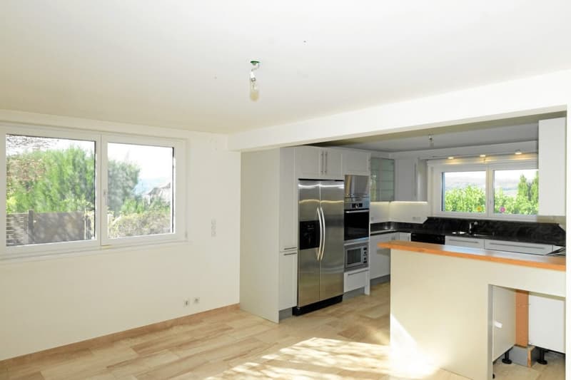 Modern kitchen with stainless steel appliances, large windows, wooden floor, and countertops