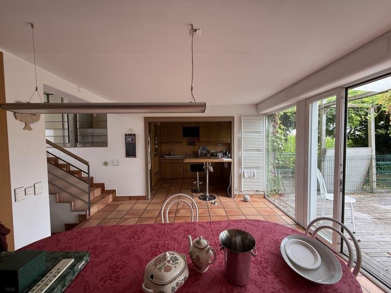Dining room with dining table, chairs, teapot, ice bucket, ceramic ware, glass doors, tiled floor, cabinet, counter, window, staircase, hanging light