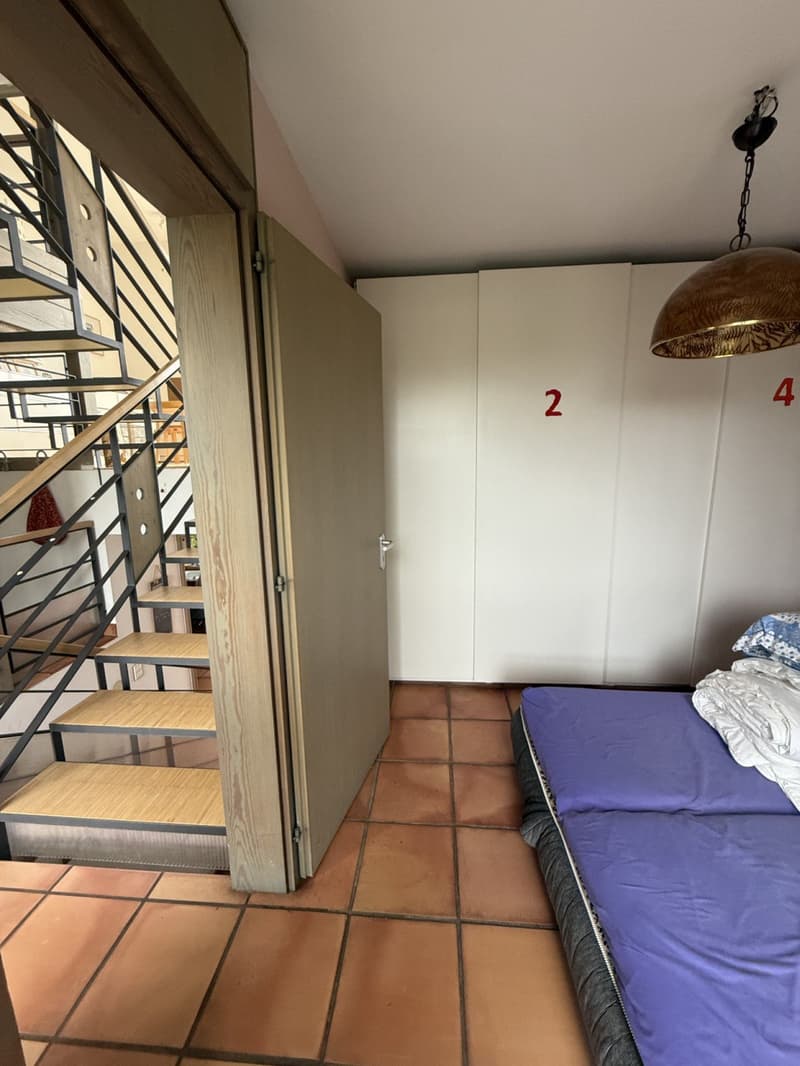 Single bedroom with a single bed, closed door, tile flooring, two closets with room numbers, a staircase on the left