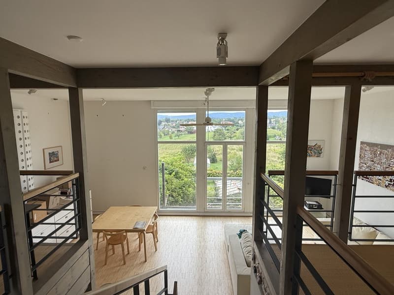 wooden floor, large windows, glass door, balcony, wooden table and chairs, ceiling fan, black railing, artwork