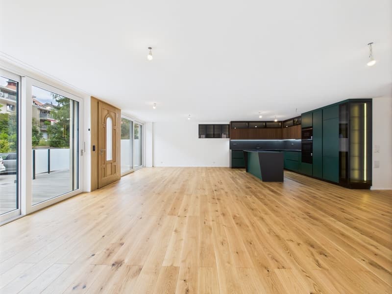 Spacious open-concept living area with hardwood flooring, large windows, and sliding glass doors leading to a balcony or terrace. The kitchen features modern green cabinets and appliances.