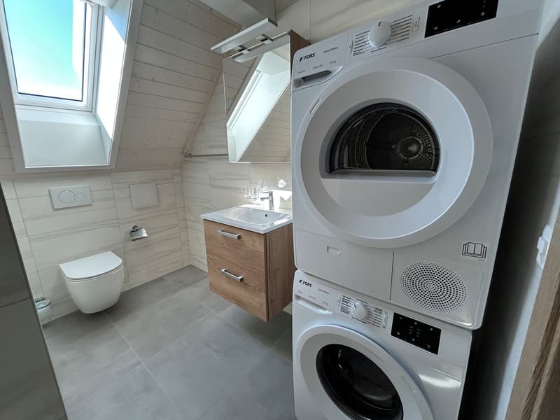 white tiled floor, wooden vanity, white toilet, stack washer and dryer, sink, mirror, skylight