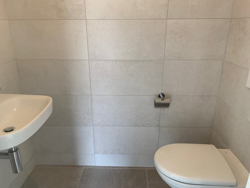 Bathroom with white sink, white toilet, tiled wall, and gray floor.