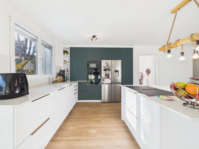 Modern kitchen, white countertops, wooden floor, green cabinets, stainless steel appliances, large window