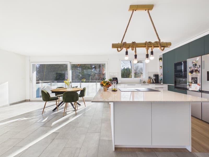 modern kitchen with island, dining table, green chairs, large windows, balcony, view of trees